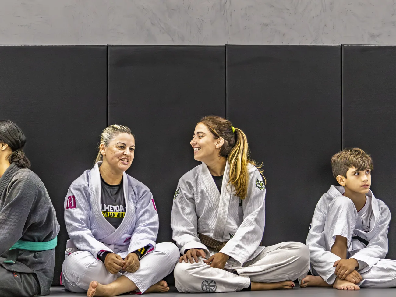 Alunas e uma criança sentados no tatame, conversando e rindo
